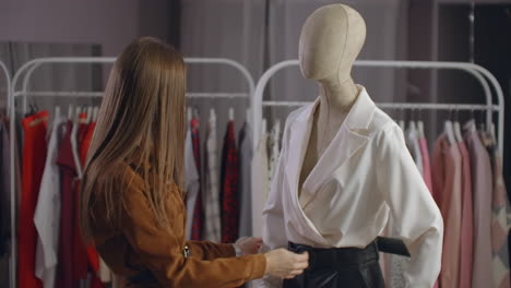 A-beautiful-girl-in-a-jacket-looks-at-clothes-on-a-mannequin-touches-and-considers-the-style-and-type-of-fabric-of-clothes-in-the-showroom.